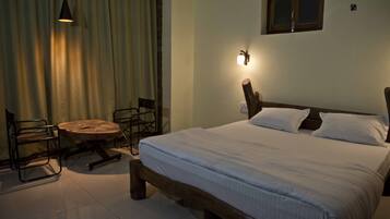 A bedroom with a wooden bed, a round table, two chairs, a hanging light, and a window with curtains.