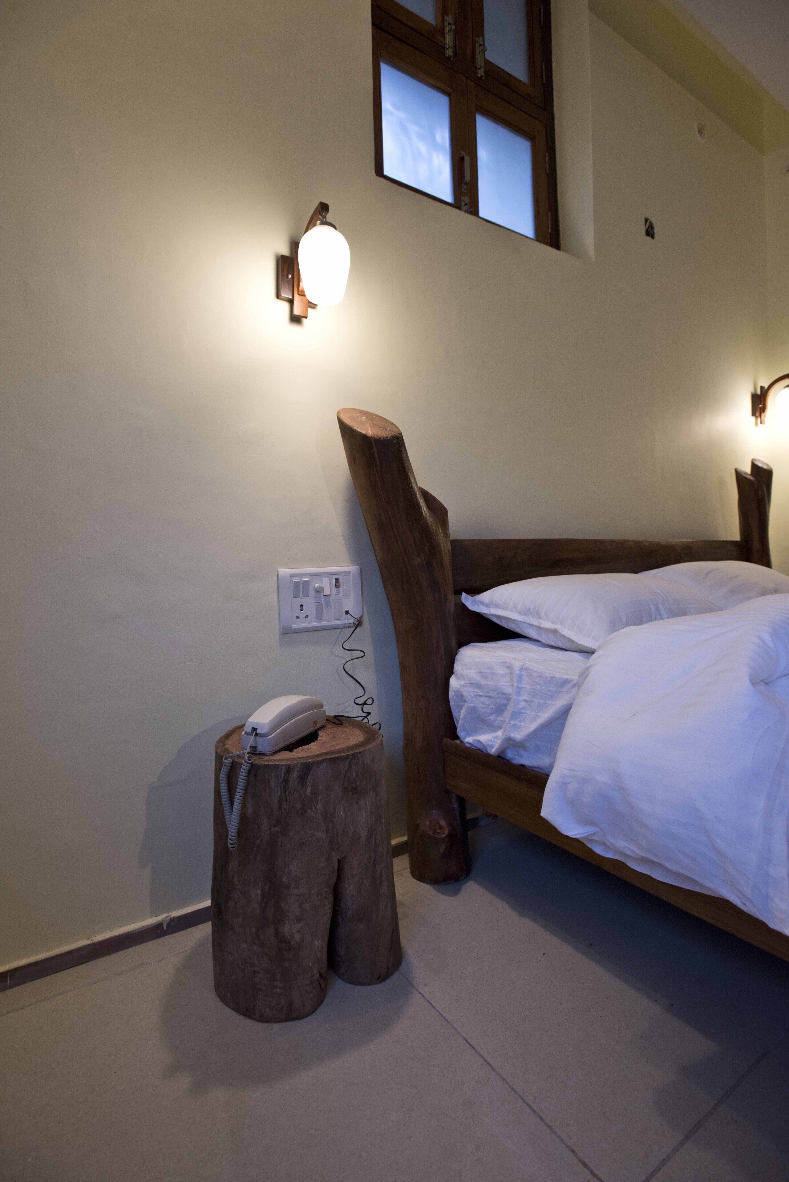A bedroom with a wooden bed frame, white bedding, a bedside telephone, and wall-mounted lighting.