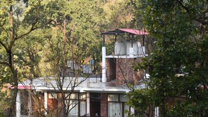 A multi-story building with a brick facade, surrounded by dense foliage. - Corbett Riviera (Lansdowne)