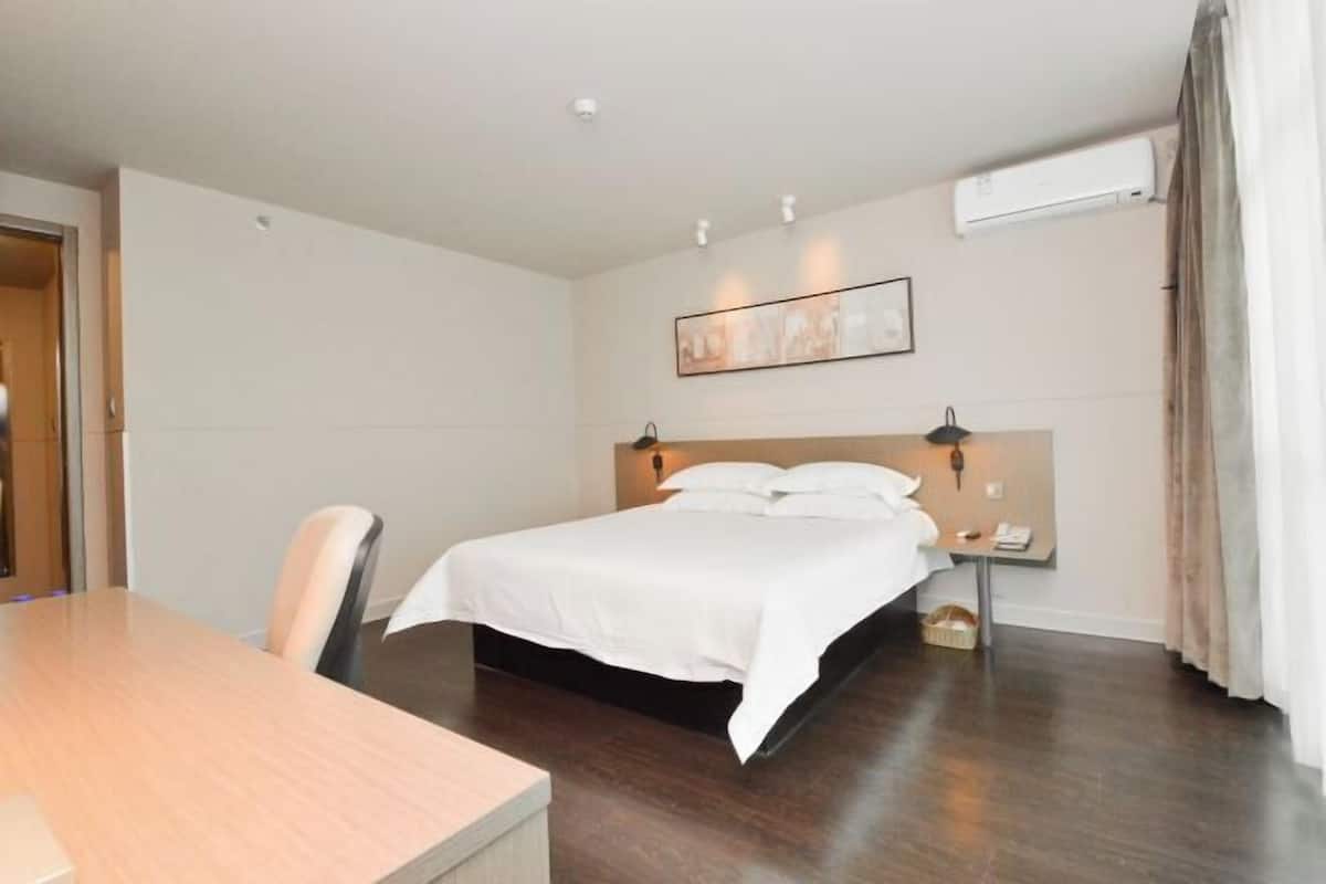 A hotel room with a bed, bedside table, lamp, and an air conditioning unit.
