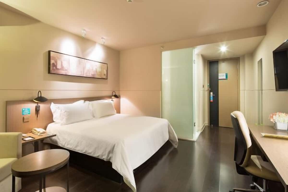 A hotel room with a bed, bedside table, lamp, chair, and a desk with a chair.