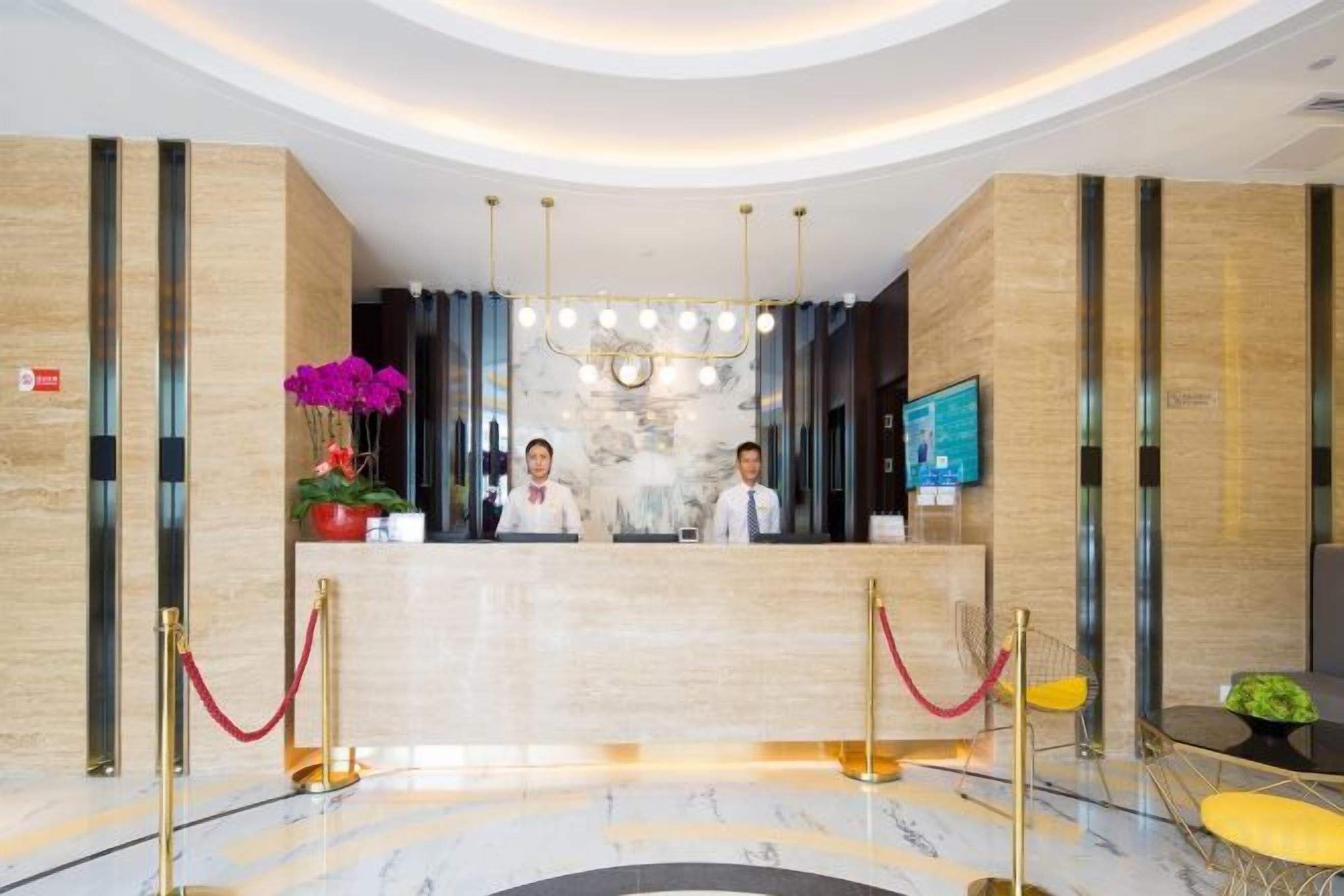 A hotel reception area with a marble floor, a reception desk, a chandelier, and a TV screen.