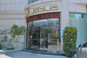A hotel entrance with a glass door, a signboard above, and a potted plant to the right.