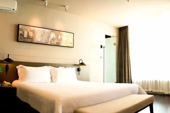 A hotel room with a large bed, a bedside table with a lamp, a wall-mounted artwork, and a window with curtains. - Jinjiang Inn Select (Sanyawan Jinjiling) (Sanya)