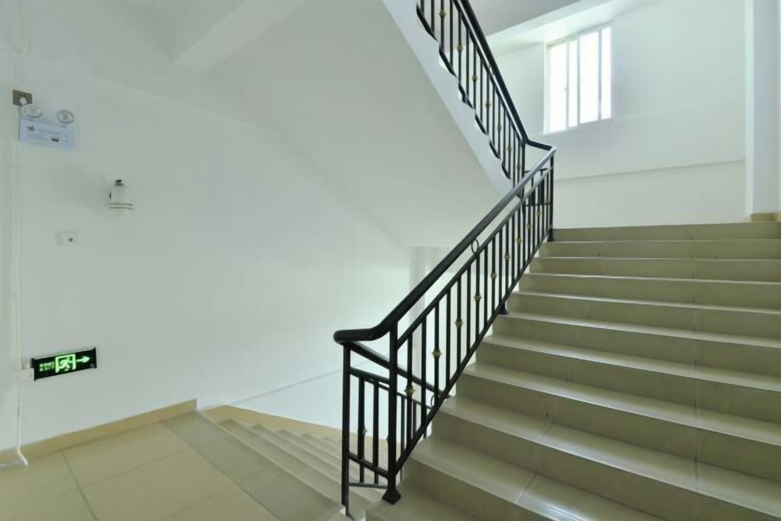A staircase with black railings and beige steps in a building with white walls.