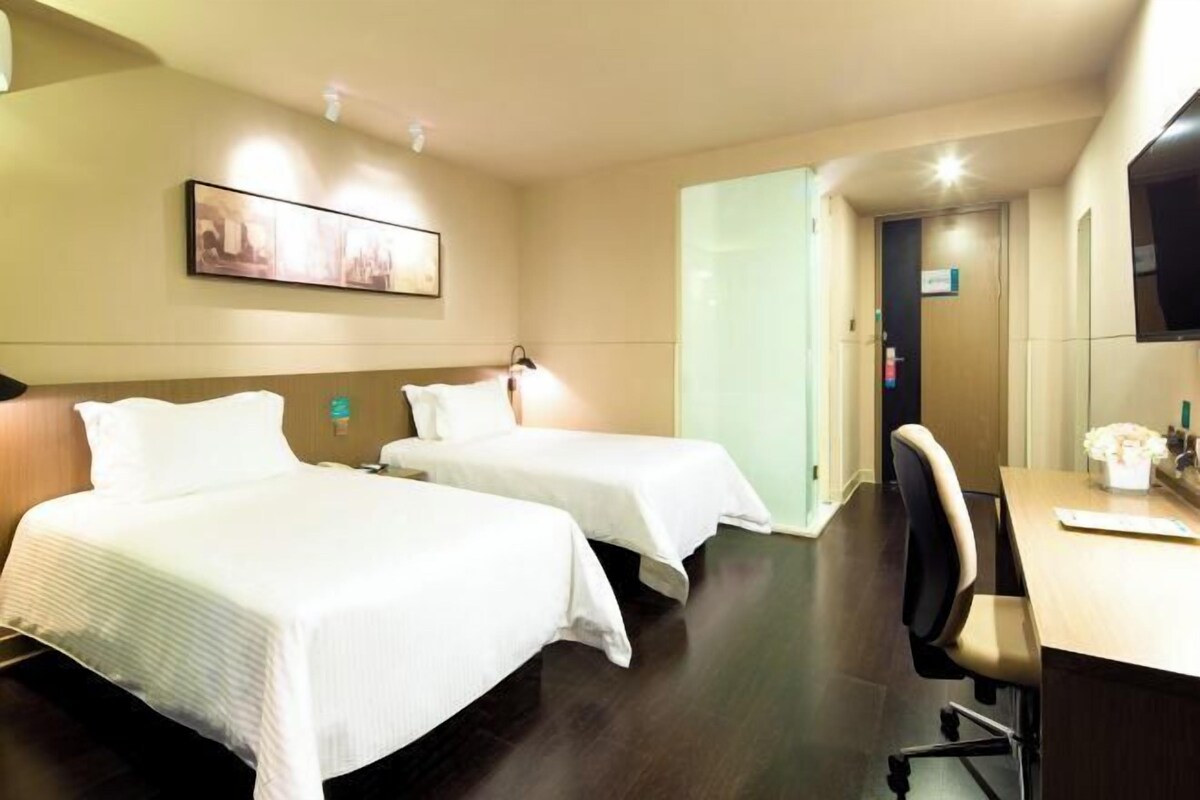 A hotel room with two beds, a desk, a chair, a television, and a painting on the wall.