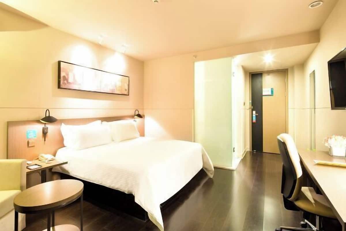 A hotel room with a bed, bedside table, lamp, chair, and a desk with a chair.