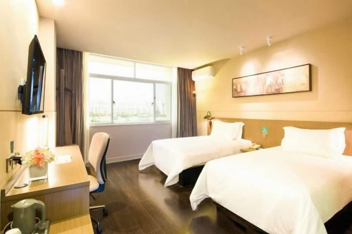 A hotel room with two beds, a desk with a chair, a coffee maker, and a window with curtains.