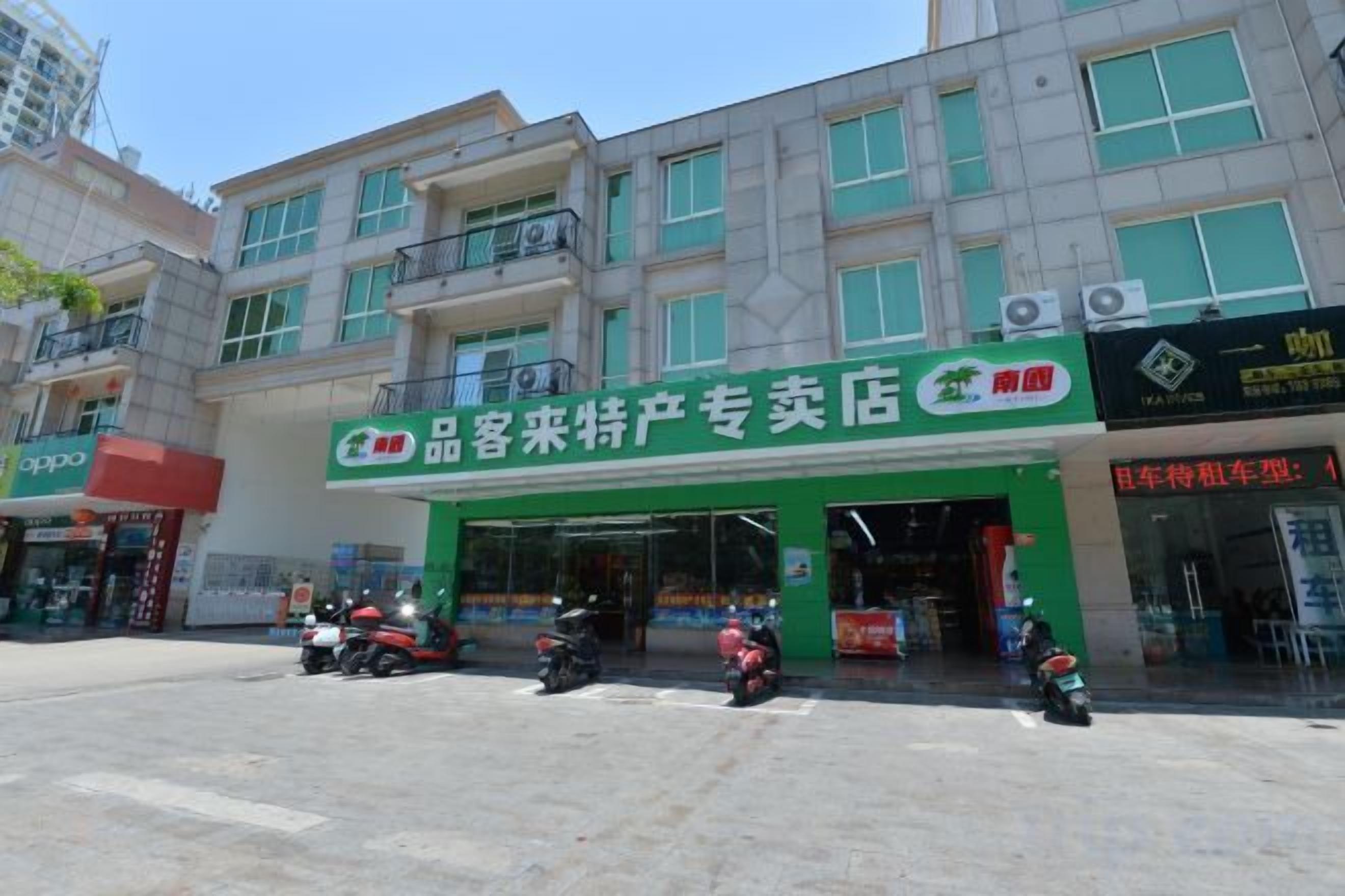 A storefront with a green sign, a motorcycle parked in front, and a building with multiple floors and windows.