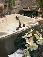 A bathtub with a modern faucet, surrounded by decorative plants and candles.
