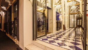 L’entrée d’un hôtel avec un sol à carreaux, de grandes fenêtres et de somptueux lustres.