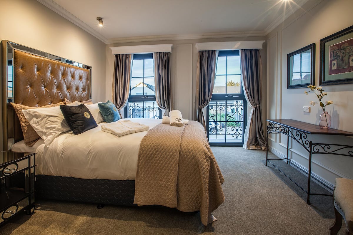 Une chambre d’hôtel avec un grand lit, une table de chevet, un petit bureau et une vue sur le balcon extérieur.