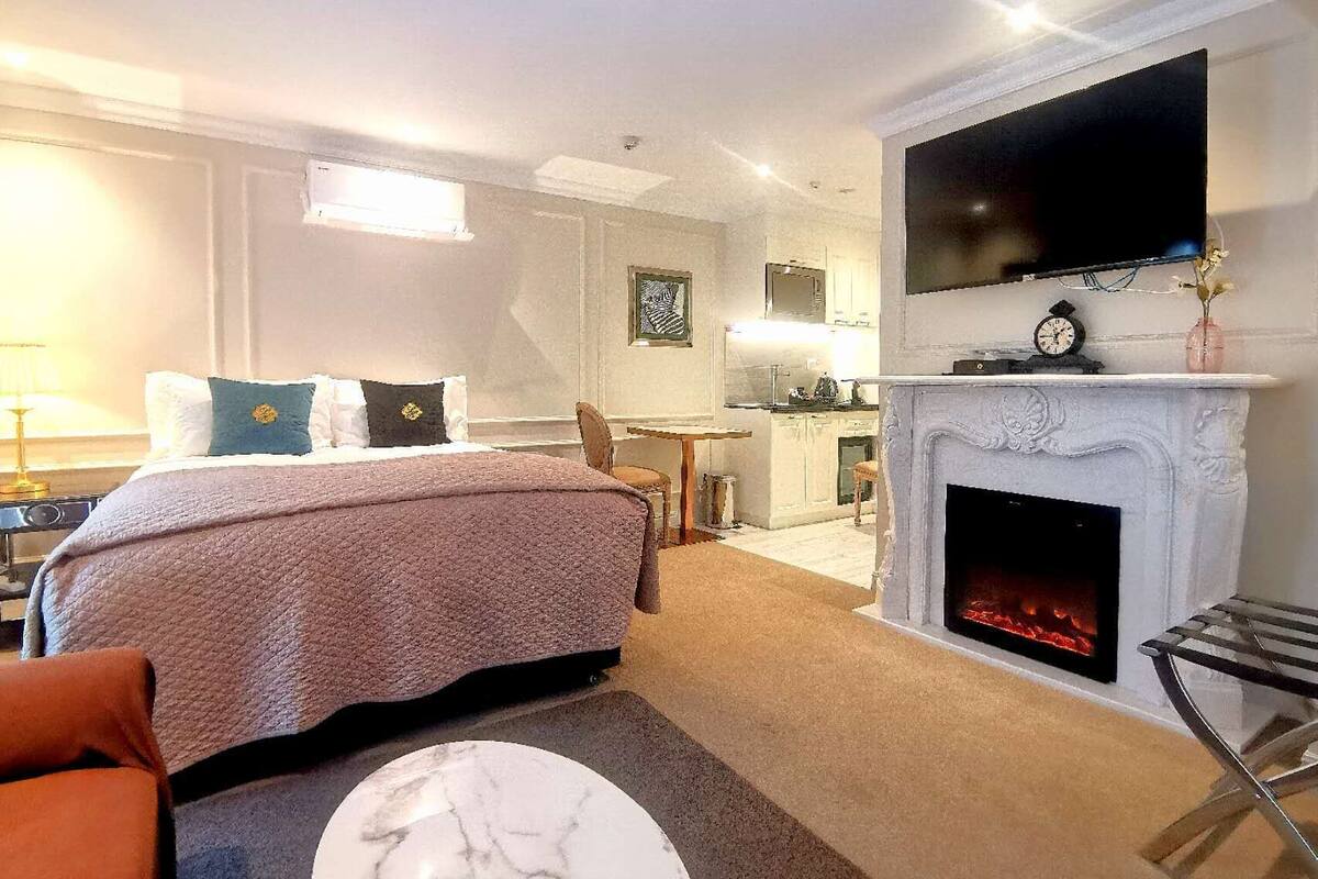 Une chambre d’hôtel avec un lit, une cheminée, un téléviseur fixé au-dessus de la cheminée et un petit coin cuisine.