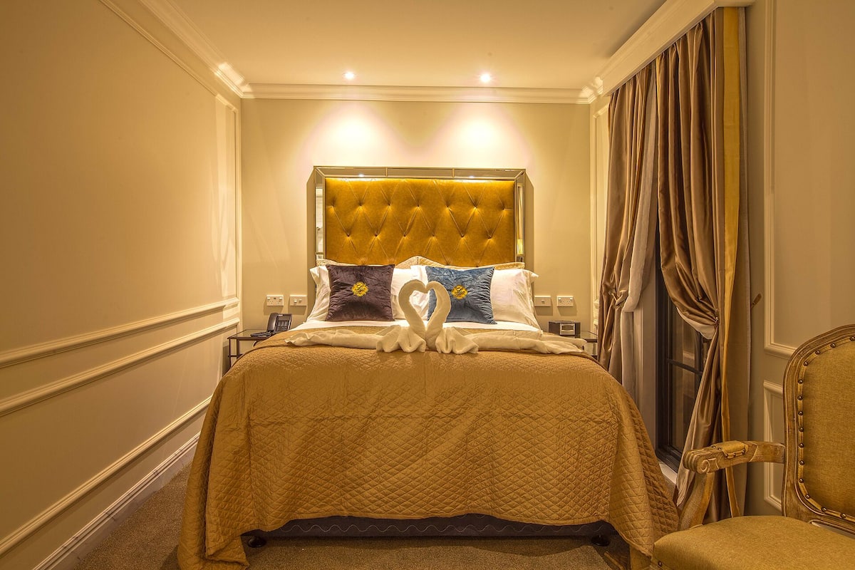 Une chambre d’hôtel avec un grand lit, une tête de lit capitonnée et une décoration en forme de cœur sur le lit.