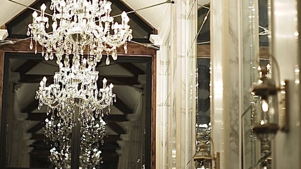 Un magnifique lustre orne un couloir, et un panneau indiquant la sortie est placé au-dessus d’une porte.