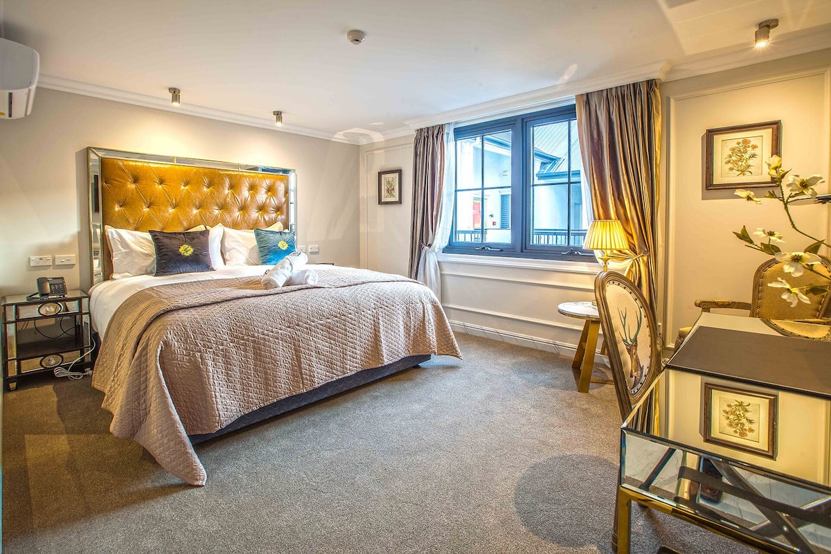 Une chambre d’hôtel avec un grand lit, un bureau avec une lampe et une fenêtre avec des rideaux.