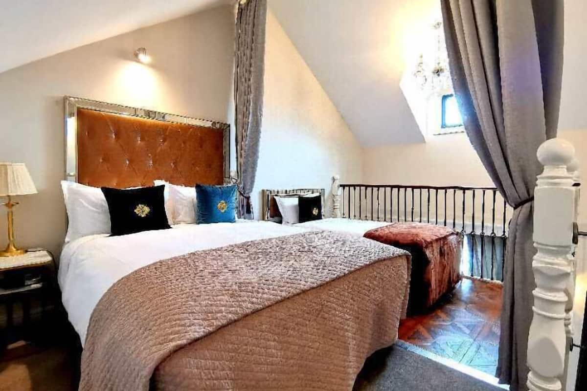 Une chambre à coucher avec un grand lit, une table de chevet, une fenêtre avec des rideaux et une balustrade de balcon.