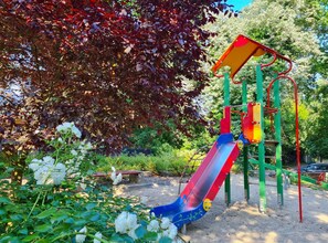 Un parque infantil con tobogán y estructuras para escalar, rodeado de árboles y flores.