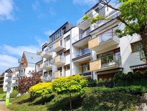 Un edificio residencial de varios pisos con balcones, un parque verde y un cielo despejado.