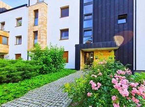 Un bâtiment moderne avec une façade en pierre, une entrée de couleur sombre et un chemin pavé menant à l’entrée.