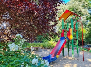 A playground with a slide and climbing structures, surrounded by trees and flowers.