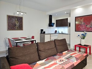 A modern living room with a sofa, a dining table with chairs, a kitchen area, and artwork on the walls. - RS2.30 - Sienkiewicz Residence (RS1, RS2) (Swinoujscie)
