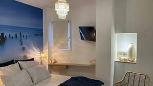 Une chambre à coucher comprenant un lit, un lustre, une télévision, une chaise et une étagère ornée d’objets décoratifs.