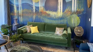 Un canapé vert agrémenté de coussins à motifs, un grand tableau abstrait et un luminaire suspendu dans un salon moderne.