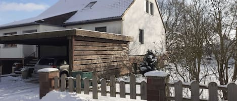 Een huis met twee verdiepingen, een garage, een houten omheining en een besneeuwde voortuin.