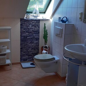 Une salle de bain avec un mur d’accent en pierre, des toilettes, un lavabo, une petite étagère avec des paniers et une plante en pot.