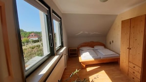 A small bedroom with a single bed, a wooden wardrobe, and a window providing a view of the outside.
