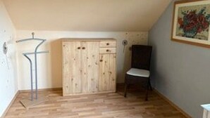 A room with a wooden wardrobe, a chair, and a painting on the wall.