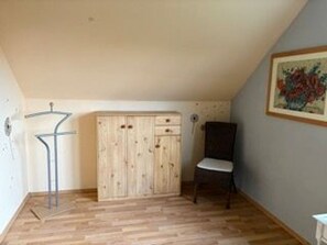 A room with a wooden wardrobe, a chair, and a painting on the wall.