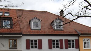 A building with a red-tiled roof, a grey door, and a blue car parked in front. - Vacation apartment Obere Stadt in the center of Weilheim (Weilheim in Oberbayern)