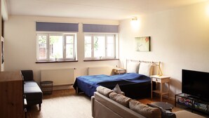 A bedroom with a bed, a sofa, a TV, a small table, and a window with a view of trees. - Vacation apartment Obere Stadt in the center of Weilheim (Weilheim in Oberbayern)