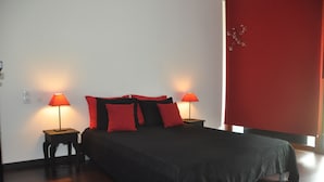 Una cama bien hecha con ropa de cama negra y roja, dos lámparas de noche y una pared de acento roja.