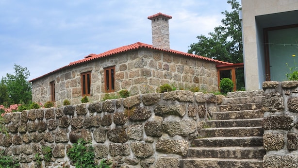 Un edificio de piedra con tejado de tejas rojas, una escalera de piedra que lleva a la entrada y un área verde al frente.