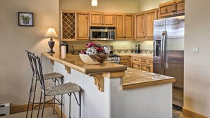 A kitchen with wooden cabinets, a stainless steel refrigerator, a microwave, and a bar area with stools. - 3 Mi to Keystone Resort: Condo w/ Mountain View (Keystone)