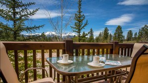 A glass-top table with two white cups and saucers, surrounded by cushioned chairs, set against a backdrop of snow-capped mountains and trees. - 3 Mi to Keystone Resort: Condo w/ Mountain View (Keystone)