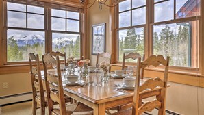 A dining room with a wooden table set for four, large windows with a mountain view, and a chandelier. - 3 Mi to Keystone Resort: Condo w/ Mountain View (Keystone)