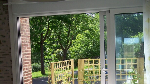 A room with a large sliding glass door leading to a garden, a round table with a remote control, and a sofa with cushions. - Authentic cottage in the countryside near Pau (Cescau)