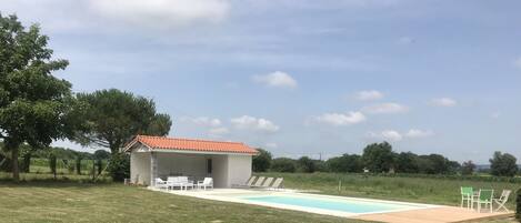 A poolside area with a covered seating area, a pool, and a garden with colorful flowers.