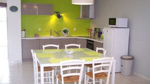 A modern kitchen with a green accent wall, white cabinetry, a white dining table with chairs, and a white refrigerator. - Authentic cottage in the countryside near Pau (Cescau)