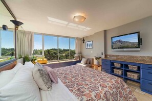 Una camera da letto con un letto grande, una TV montata a parete e vista all'esterno tramite ampie finestre.