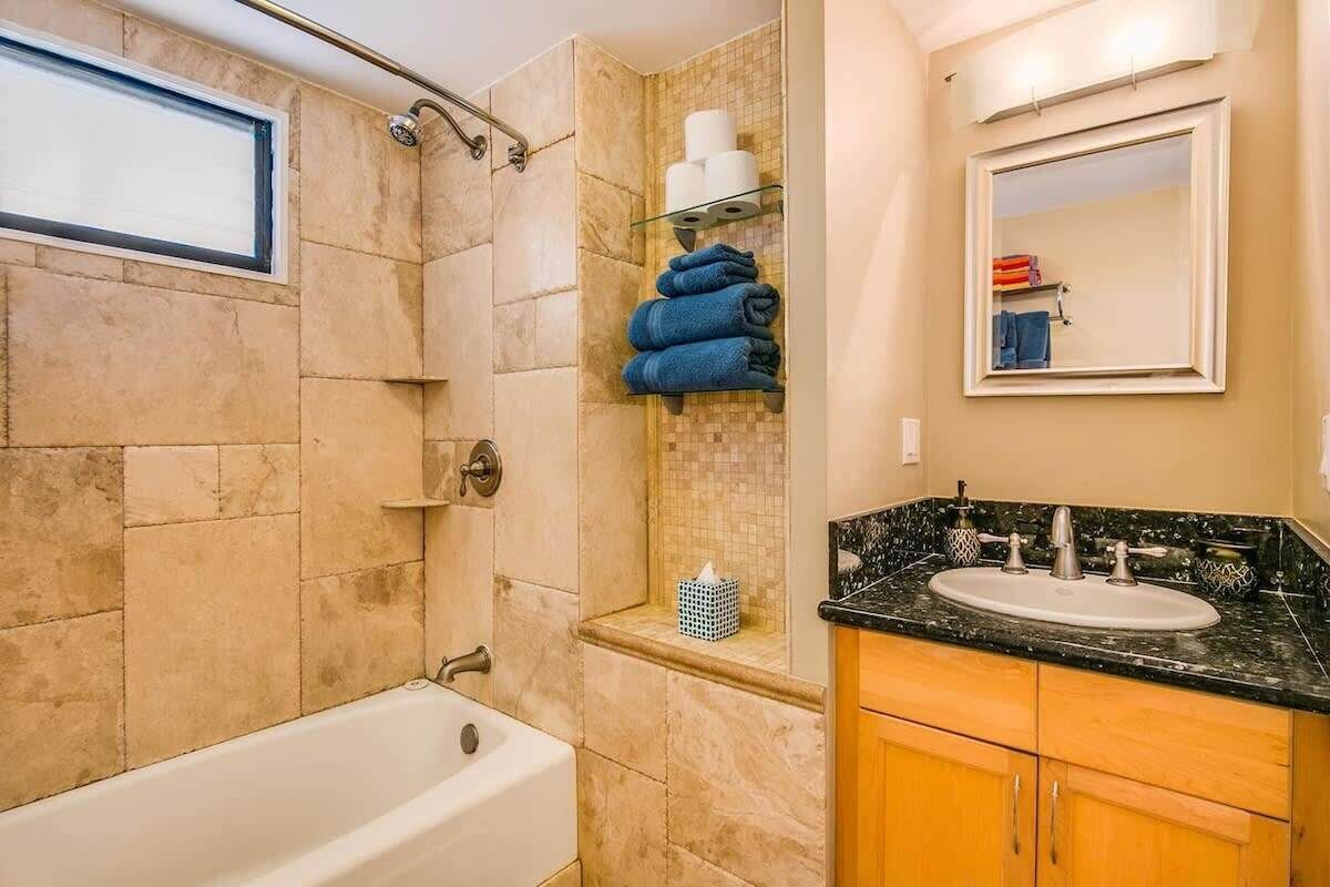 A bathroom with a bathtub, a sink with a vanity, a shower area, and a shelf with towels.