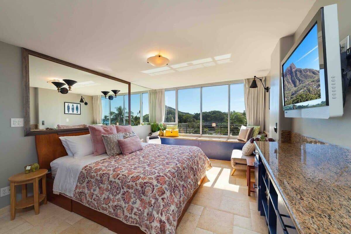 A bedroom with a large bed, a TV mounted on the wall, and a view of the outdoors.