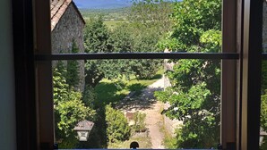 A view through a window of a garden with a stone building, a clear sky, and distant mountains. - Charme D'un mas en Luberon, Calm, Panoramic view, Swimming pool, Fireplace (Lacoste)