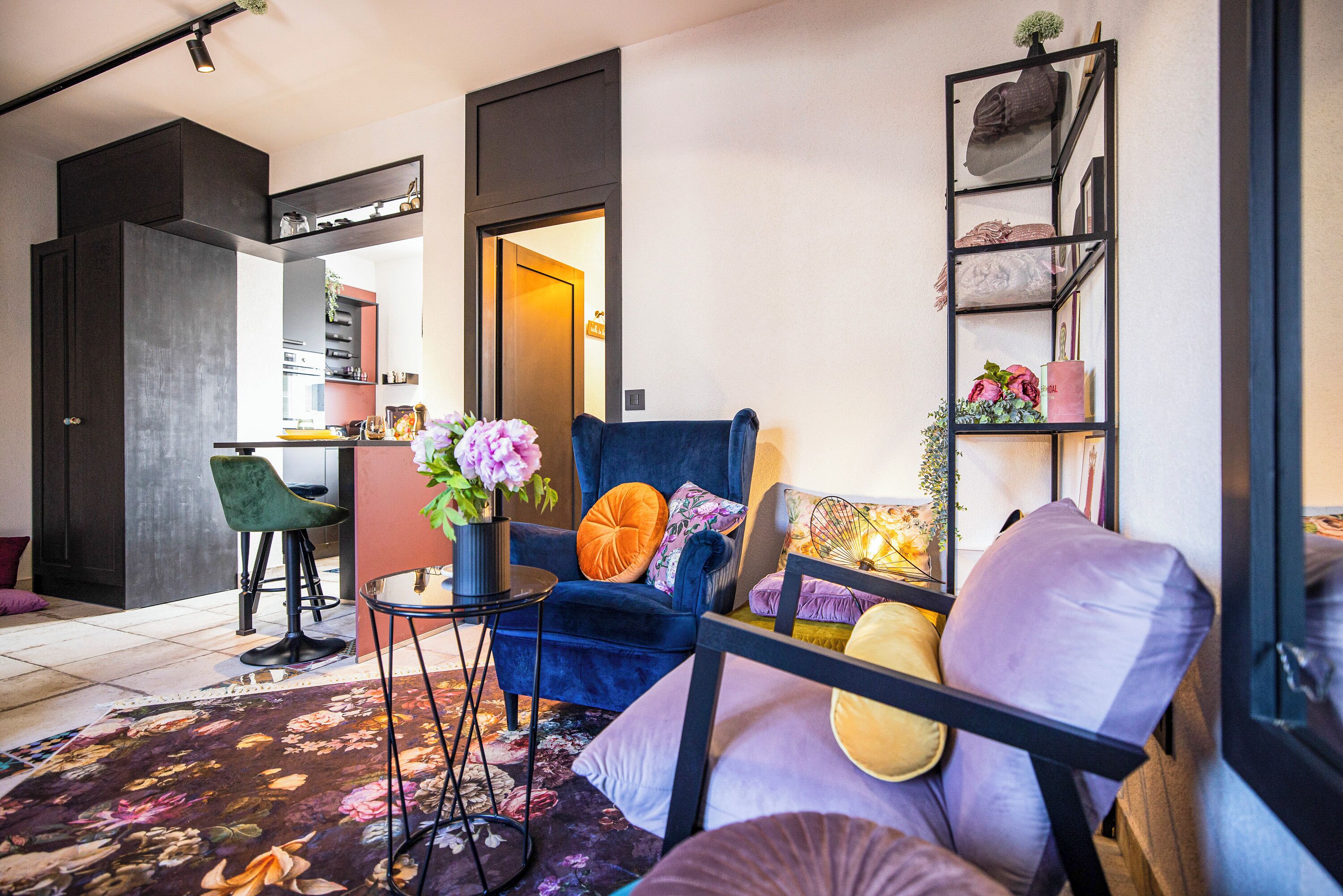 Un salon moderne avec un canapé bleu, une petite table d’appoint sur laquelle est posé un vase de fleurs, et une bibliothèque adossée au mur.