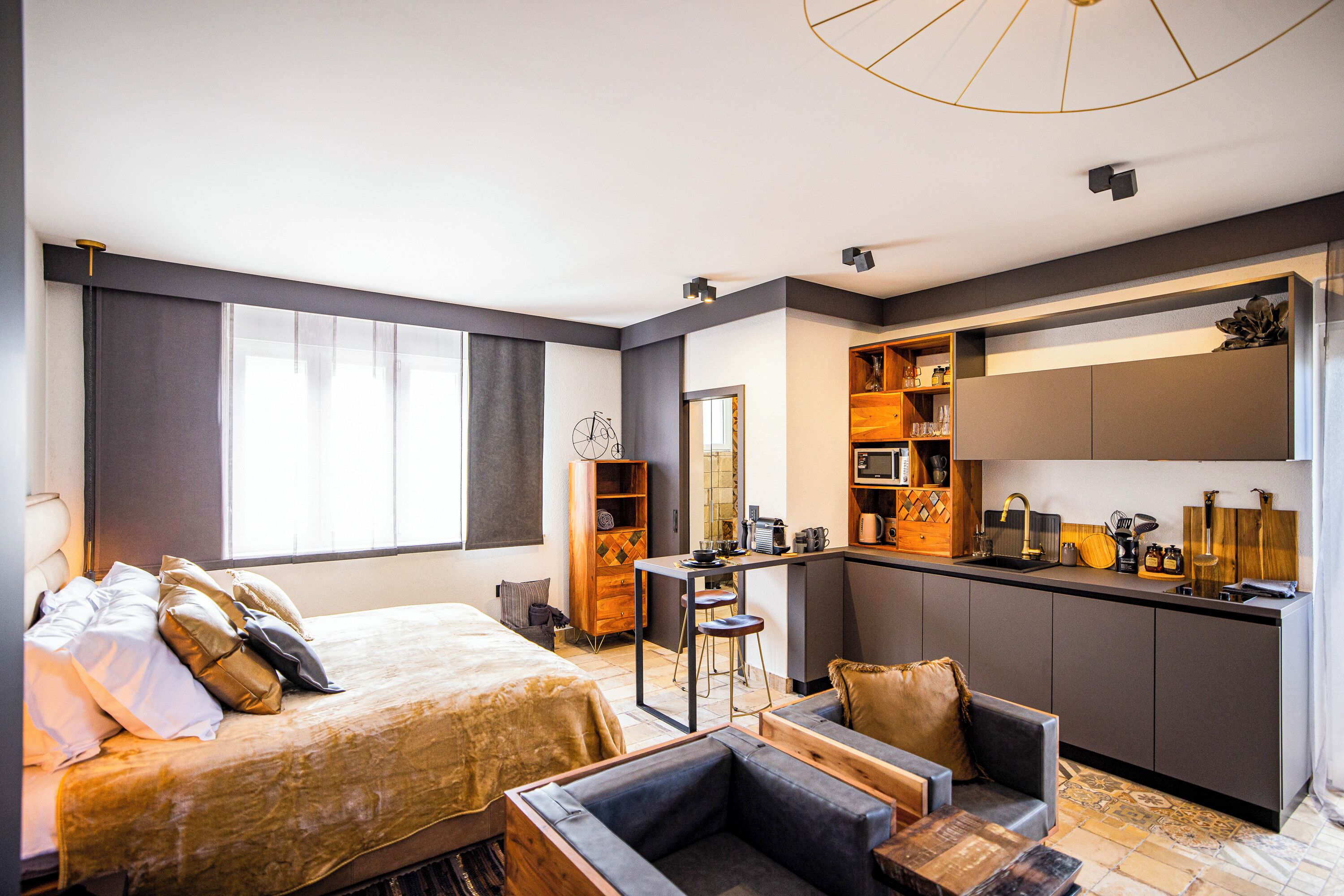 Una habitación de hotel moderna con una cama grande, una zona de estar, una kitchenette y un baño.