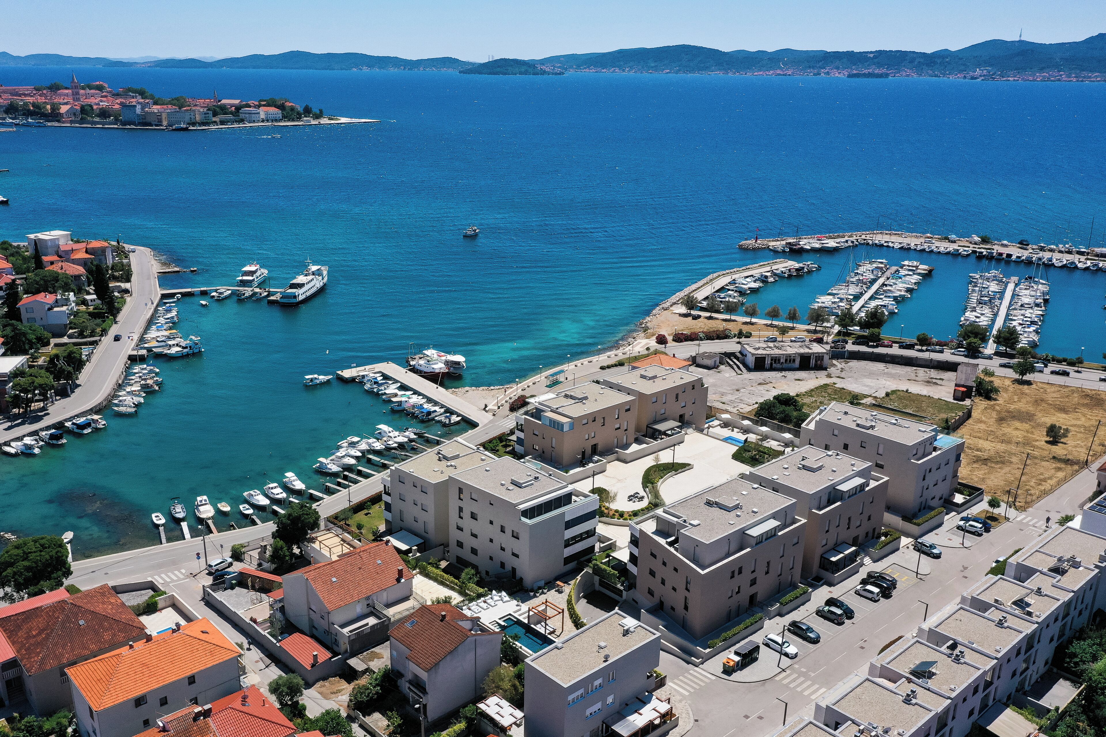 A coastal town with modern buildings, a marina with boats, and a clear view of the sea.